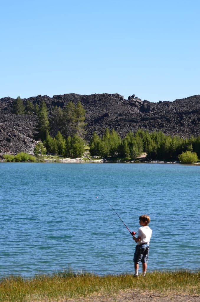 A boy fishing at Butte Lake with lava beds in the background. Lakes in Lassen Park
