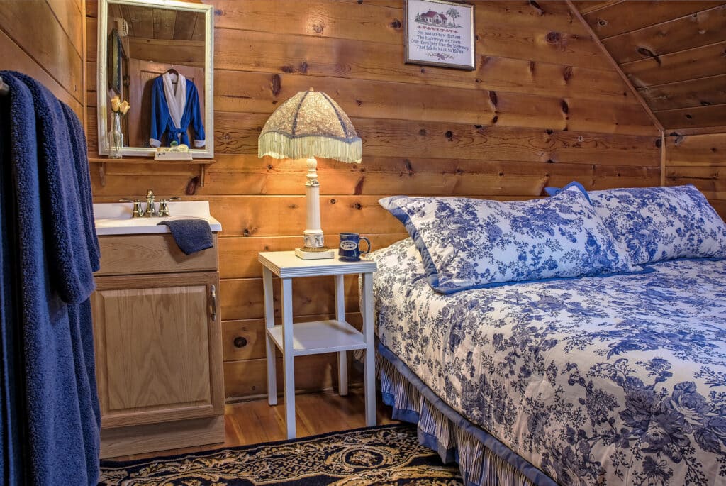 The Bluebird Room at St Bernard Lodging with blue and white bedding, sink, mirror, and log cabin walls.