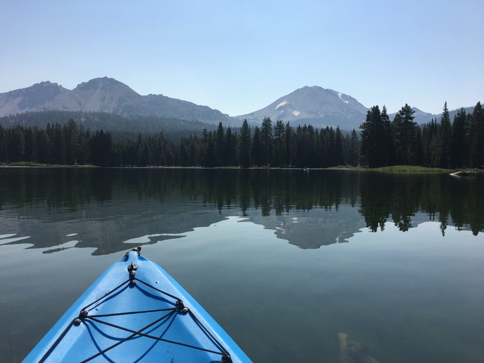 Tip of Blue Kayaking on the calm water of Manzanita Lake with reflection of the mountains in water.