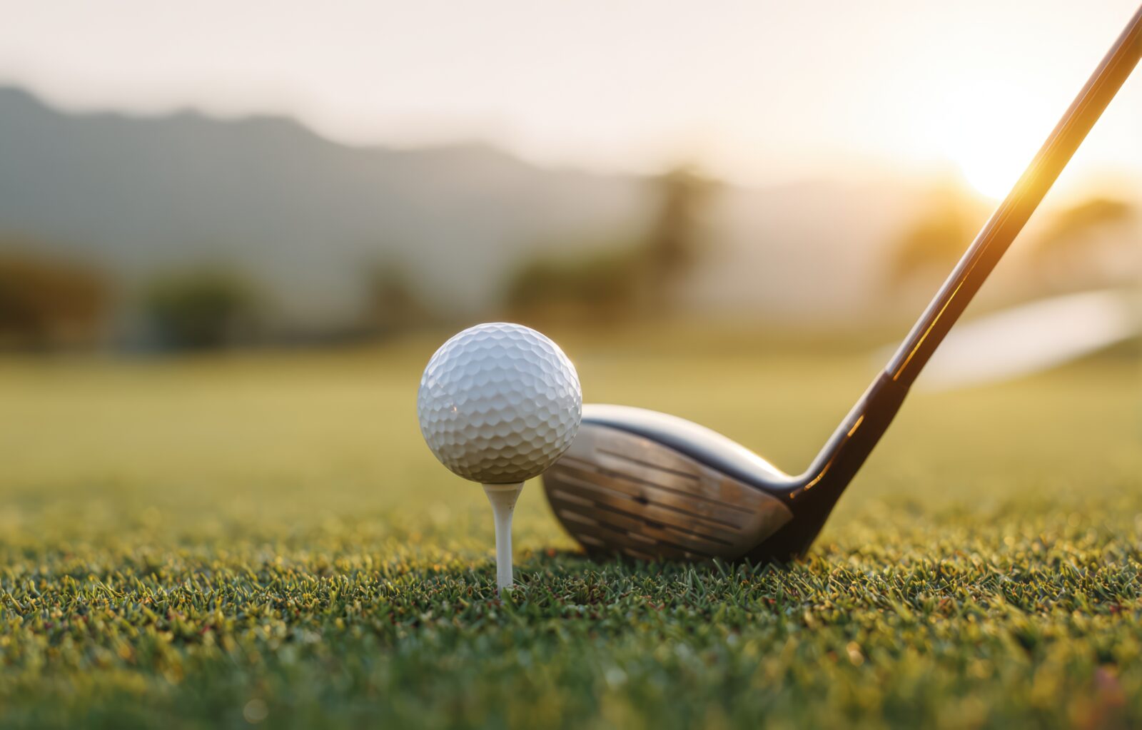 Close up shot of golf ball on tee, club behind it as the sun sets over the hills. Bailey Creek Golf Course